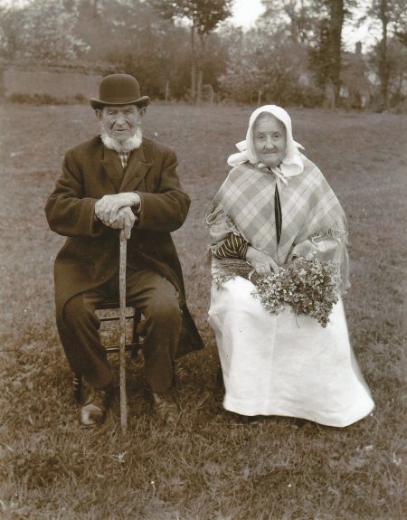 B&W photograph of Peter and Mary Minns of Lower Radley in their best clothes pictured sitting in a field in about 1902 (Mrs Minns is holding a bouquet of flowers, so perhaps a special occasion such as a wedding anniversary)